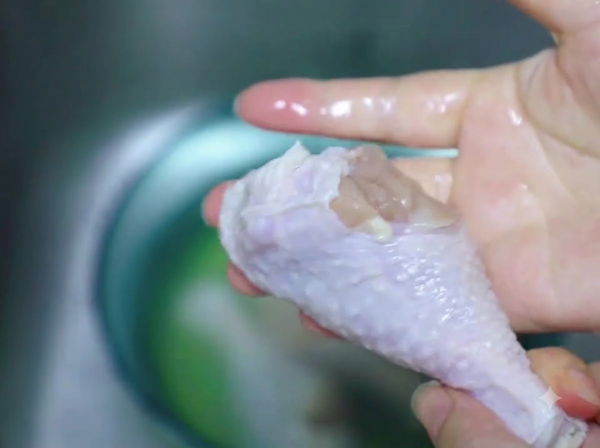 A thawed chicken drumstick being wiped dry with a paper towel.