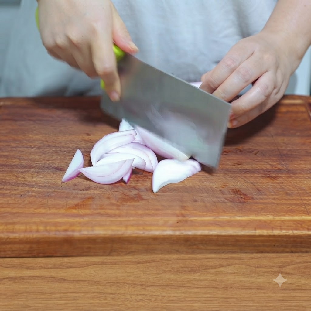 A kitchen knife slicing an onion into thin shreds on a wooden cutting board.