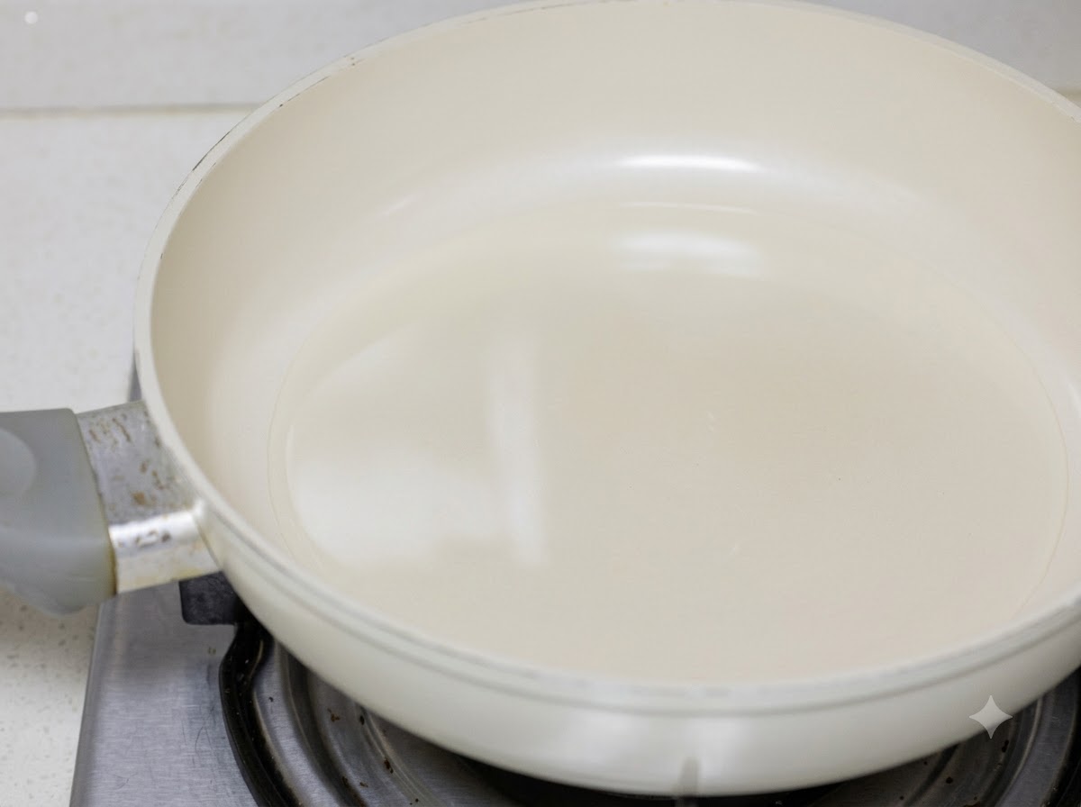 Chicken pieces being pan-fried in cooking oil inside a white pan.