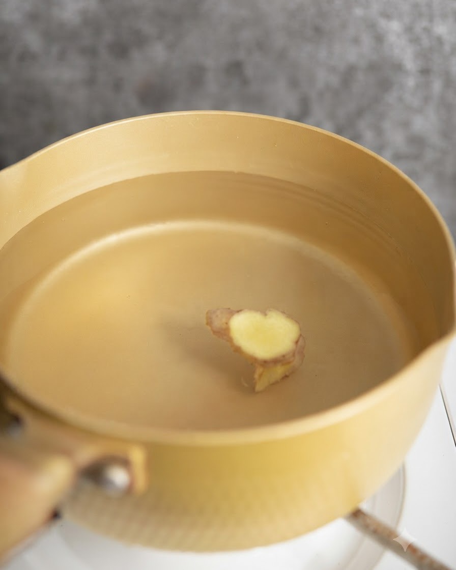Chicken pieces being blanched in a pot of water with ginger slices.