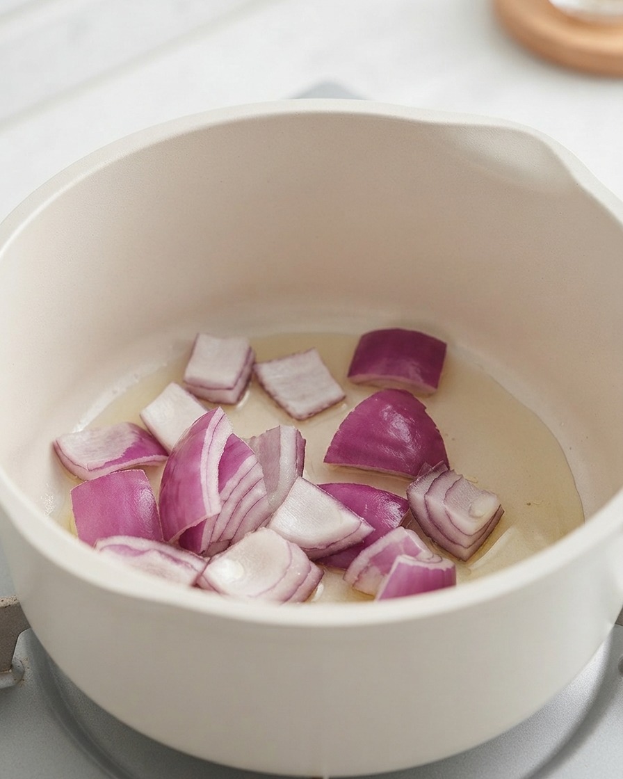 Chopped red onions and potatoes cooking inside a white pot.