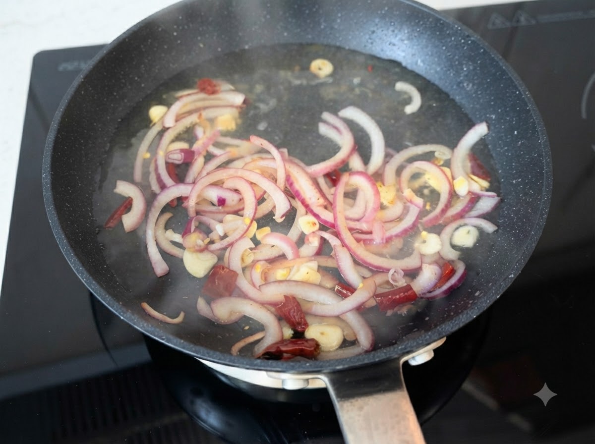 Hot water being poured over sautéed red onion slices, garlic, and chili peppers in a pan.