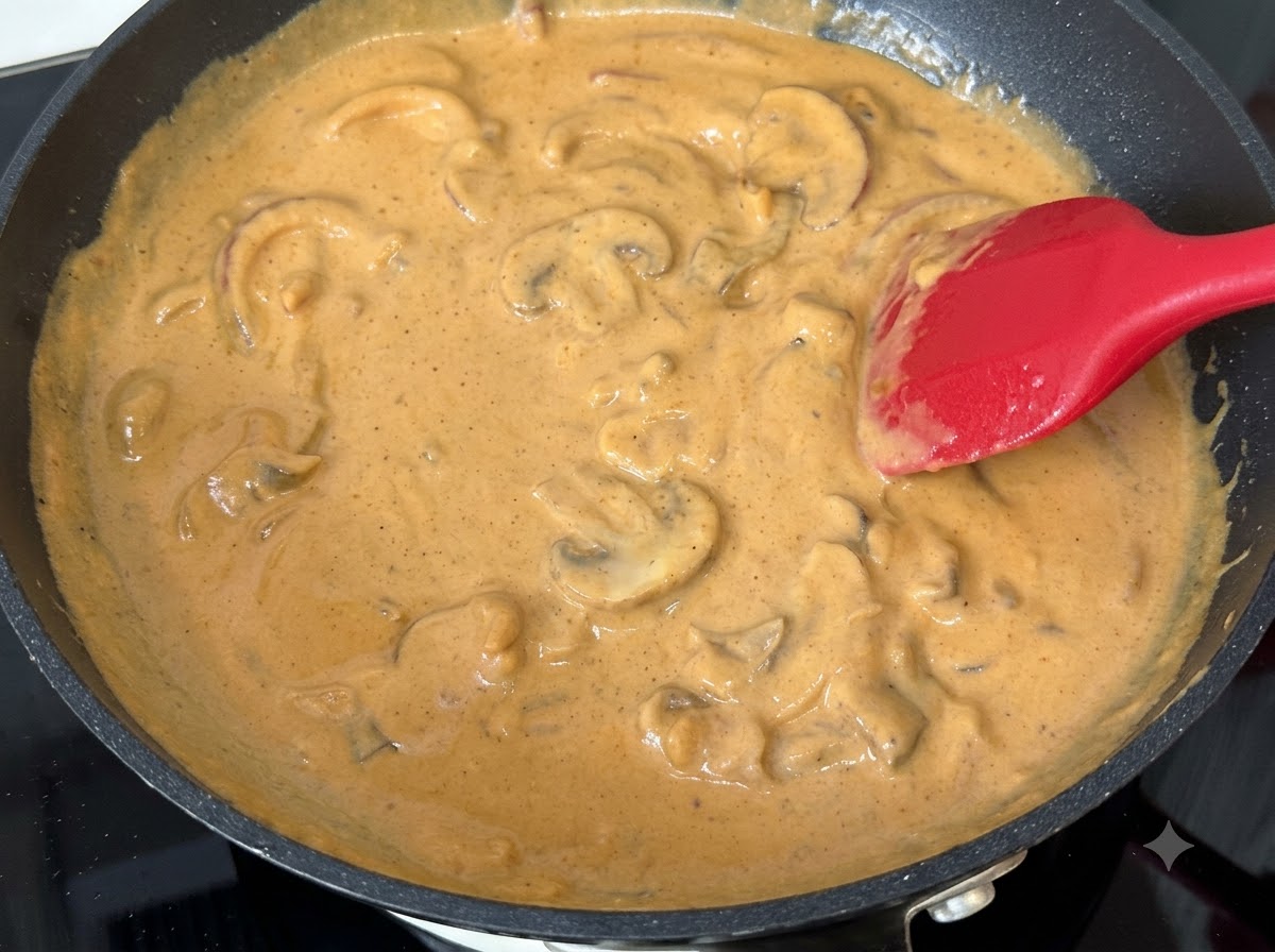 Slices of mushrooms mixed into simmering curry cream sauce in a pan.