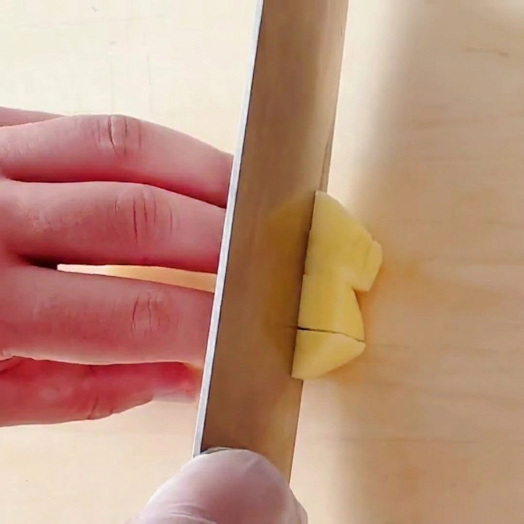 Potatoes being chopped into small square cubes on a wooden cutting board.