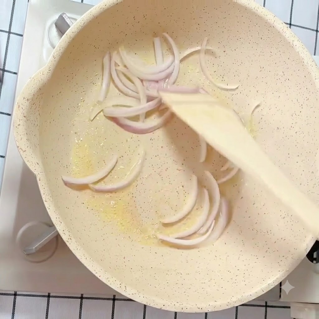 Sliced white and purple onion strips being stir-fried in a buttered pan with a wooden spatula.