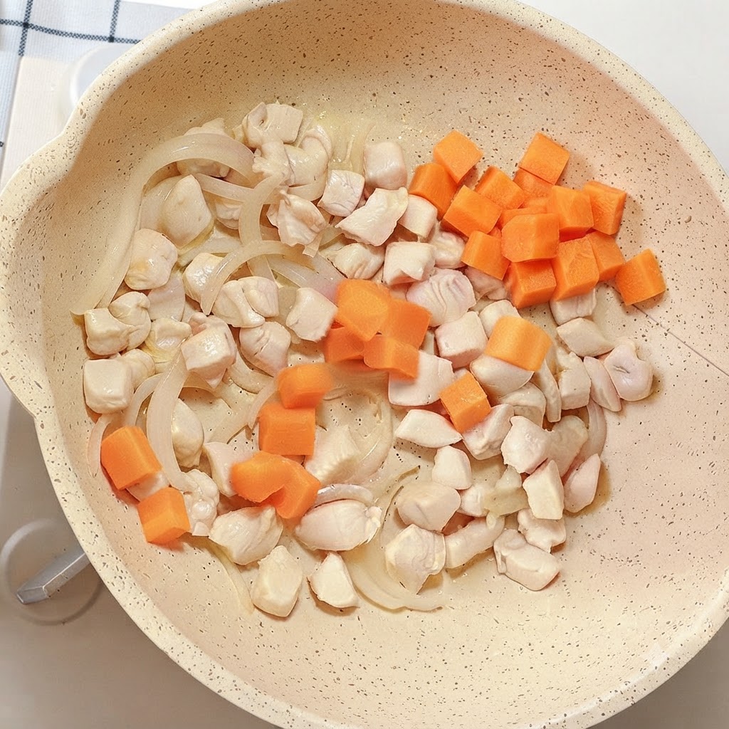 Bright orange carrot cubes added to the pan containing chicken and onions.
