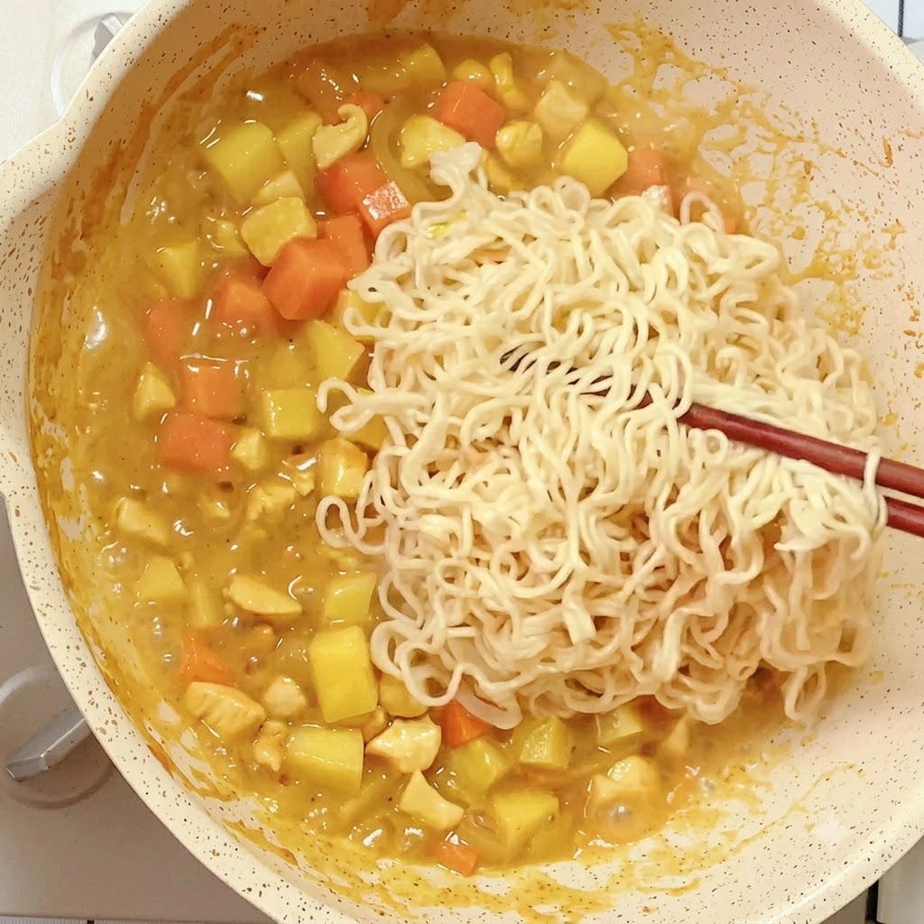 Pre-cooked instant noodles being placed with chopsticks into a pan of reducing curry mixture.