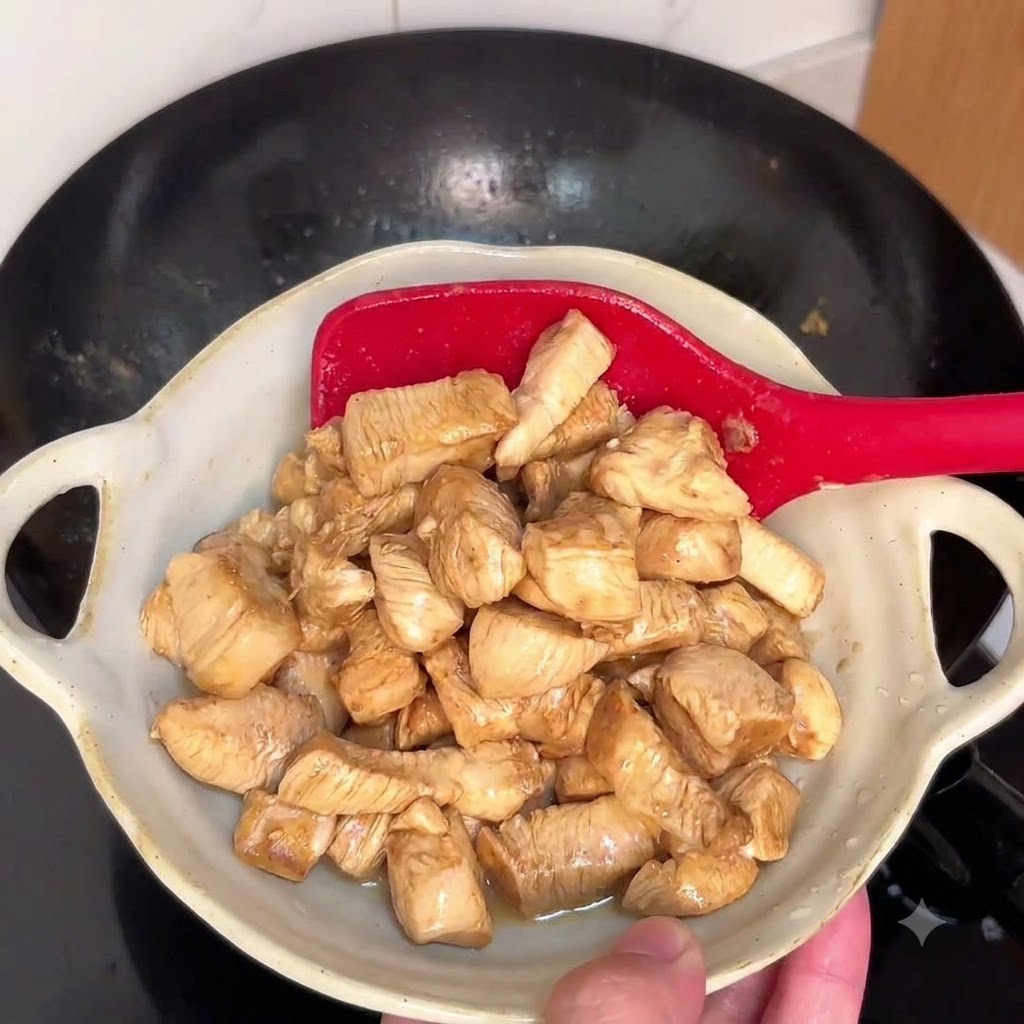 Chicken pieces stir-frying in a hot wok with a red spatula.