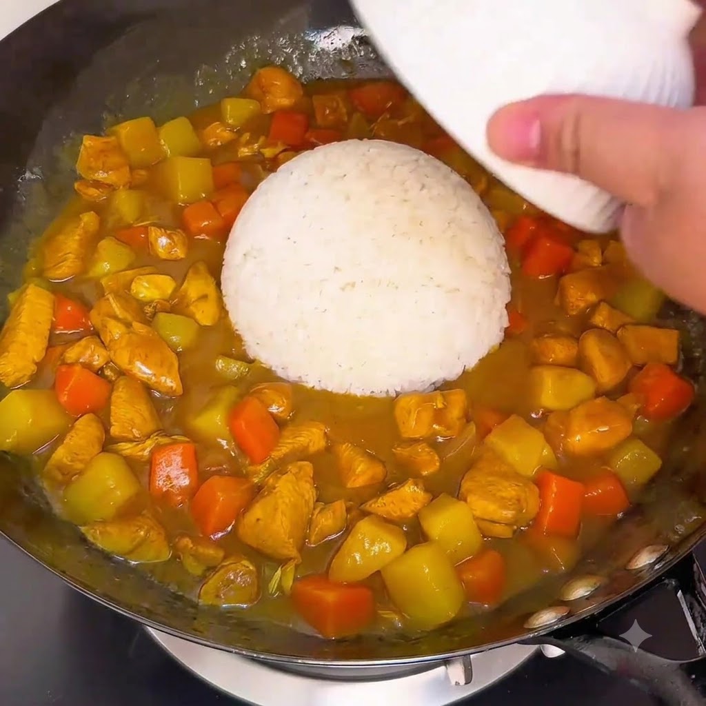 A bowl of white rice being inverted into the simmering curry sauce in a wok.