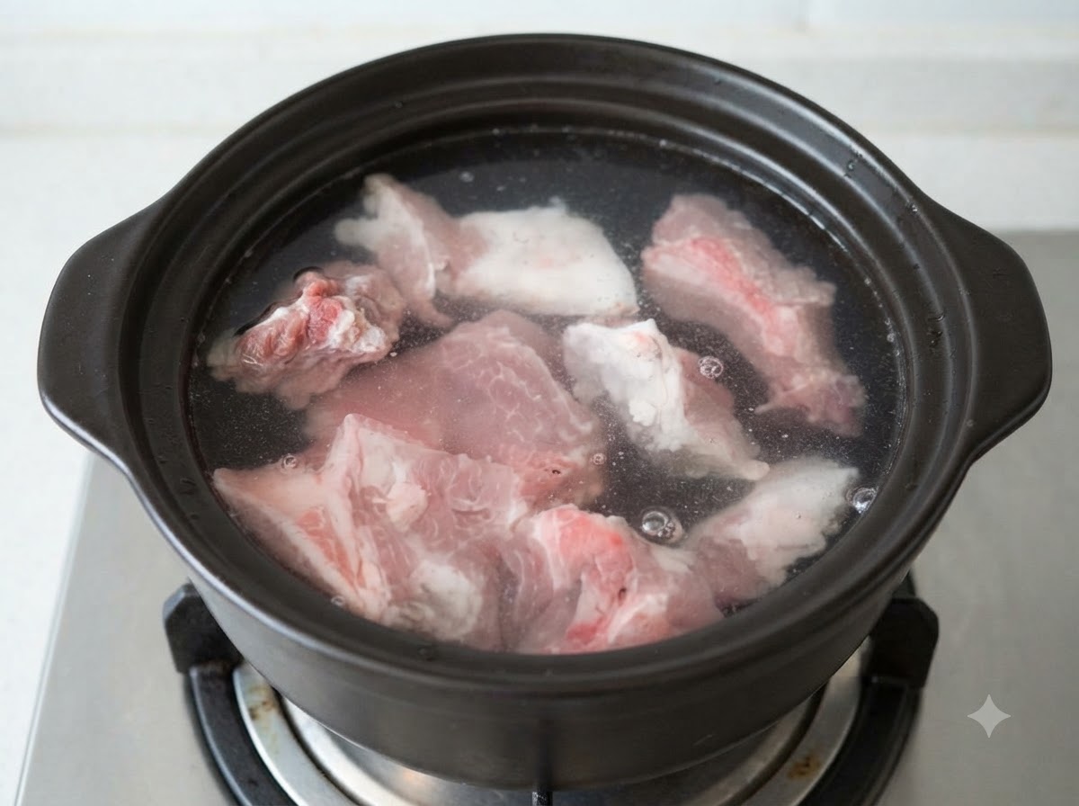 Raw pork bone pieces submerged in cold water inside a dark clay pot.
