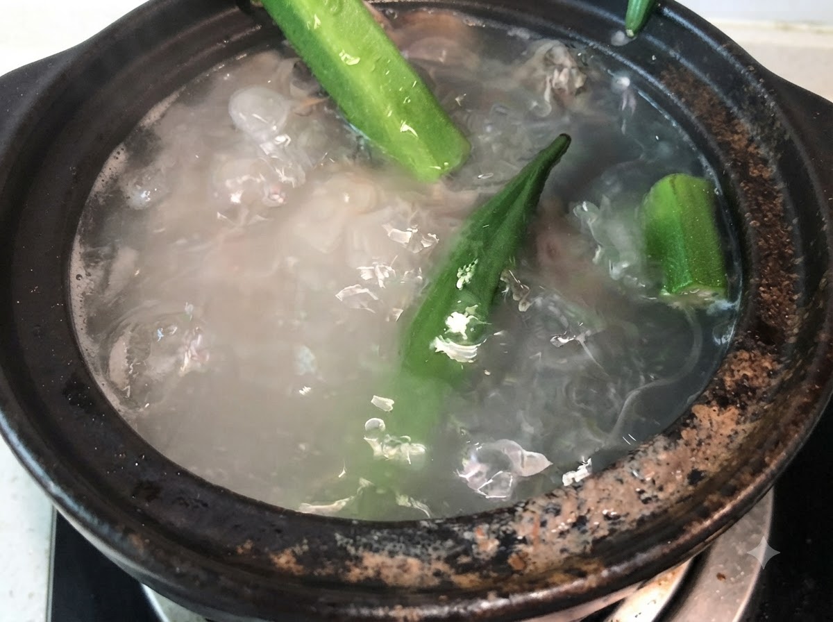 Whole green okra pods being added into boiling pork bone broth.