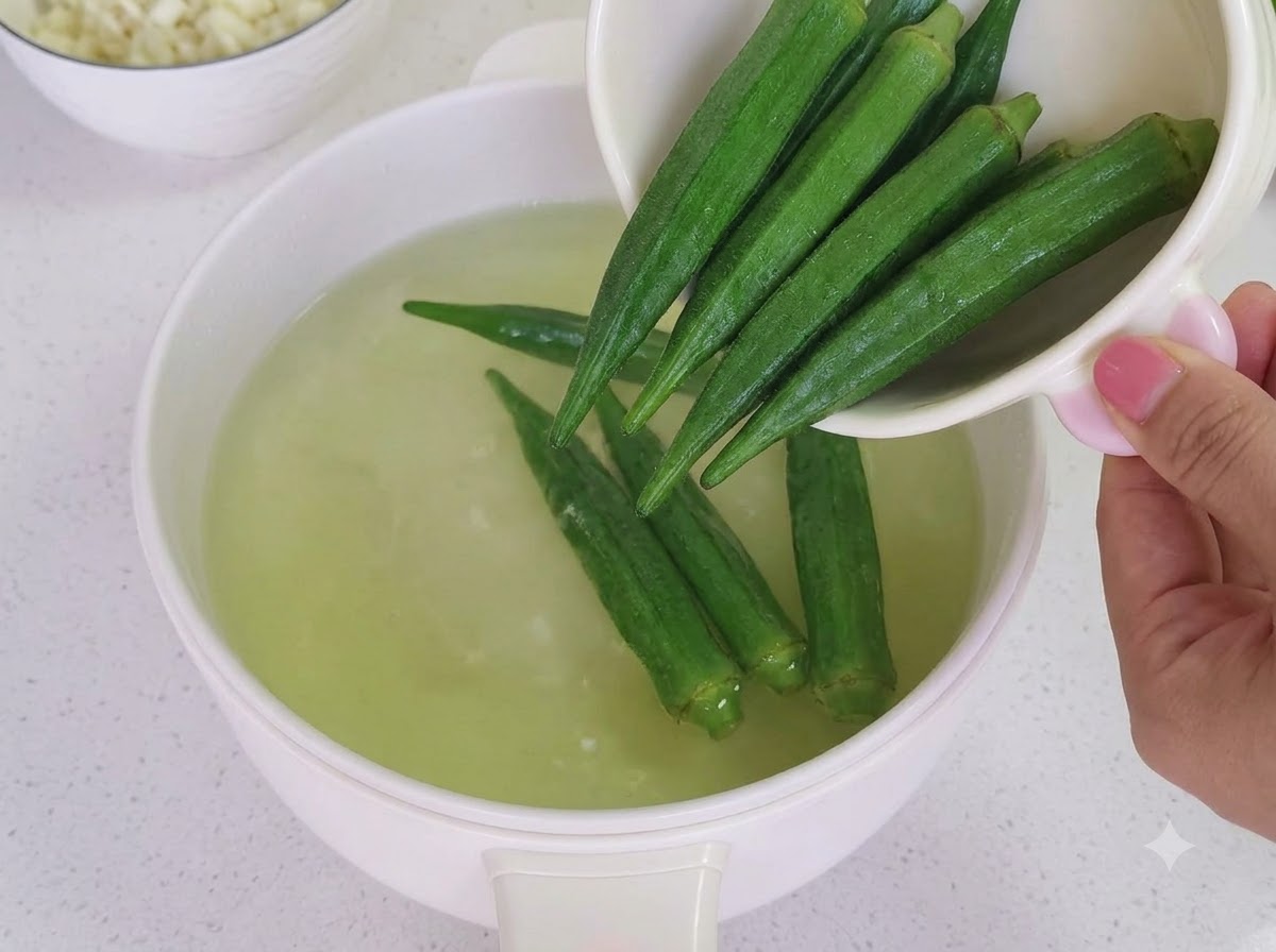 Cooked okra being cut into small segments on a wooden cutting board.