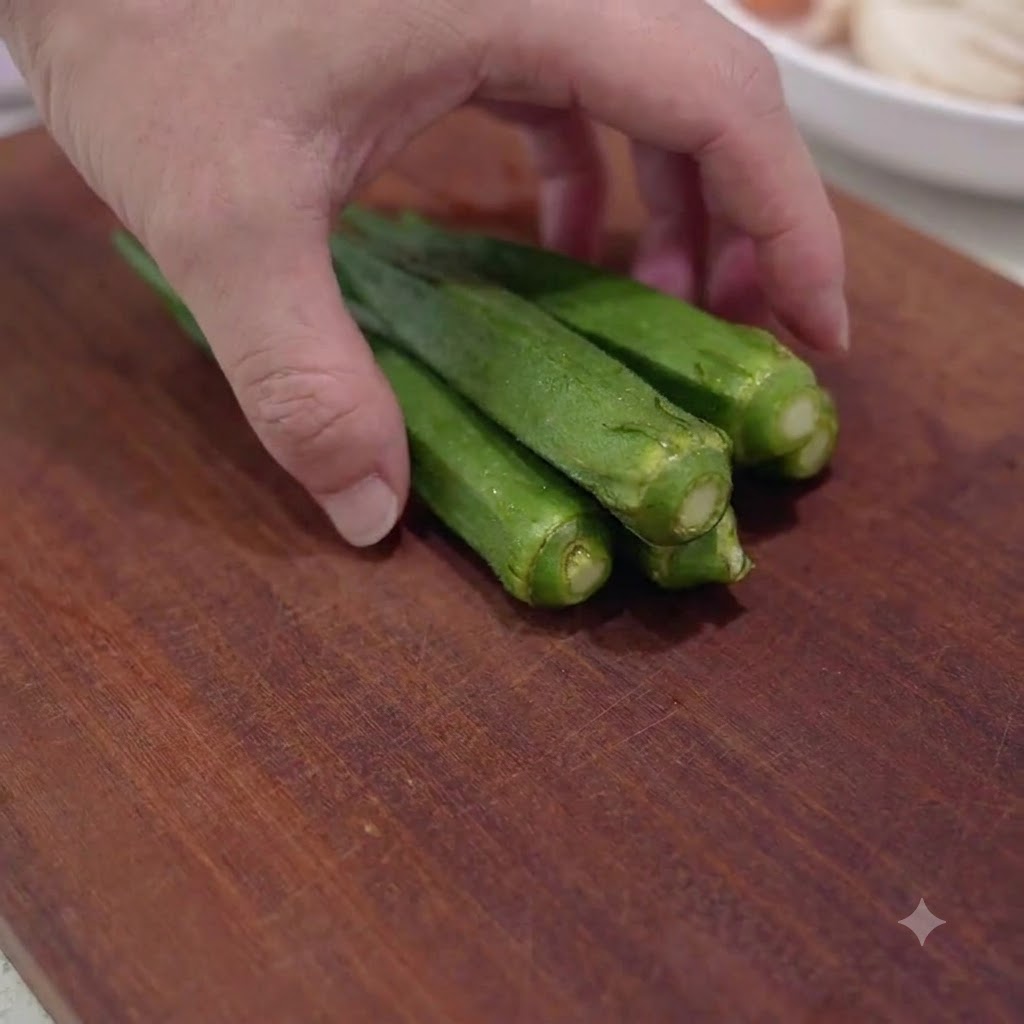 Fresh green okra pods being sliced into small pieces on a wooden cutting board.