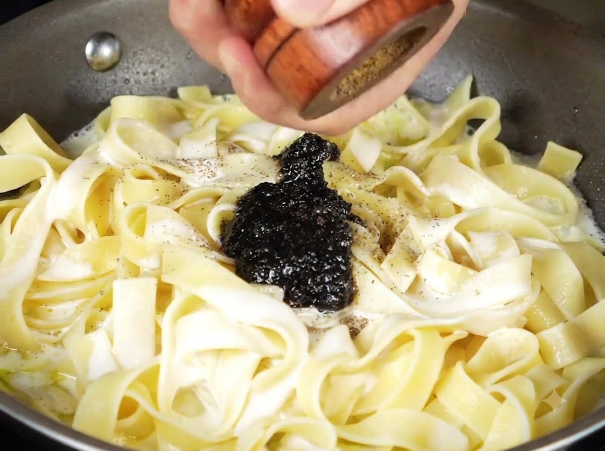 Black truffle sauce and freshly ground black pepper sitting atop the creamy pasta in the pan.
