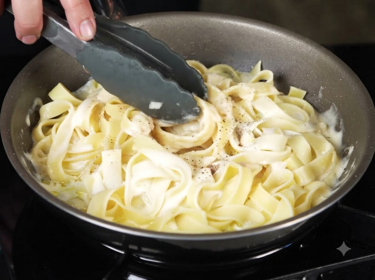 Tongs tossing and mixing the creamy black truffle pasta together in the pan.