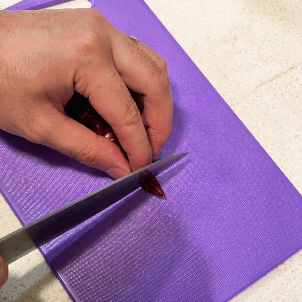 Slicing garlic cloves and cutting dried chili peppers into sections on a purple cutting board.