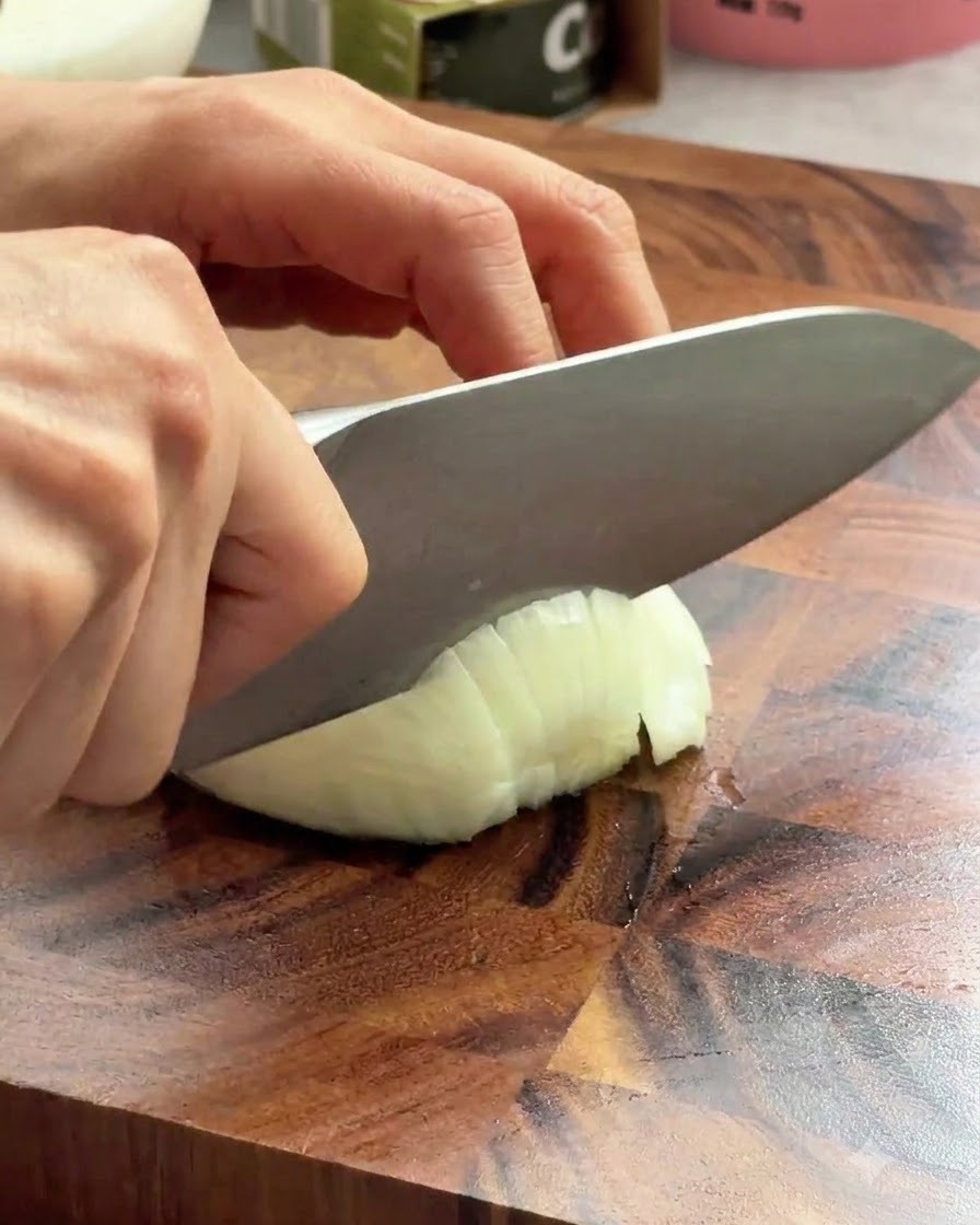 A sharp chef knife slicing through a white onion on a wooden board.