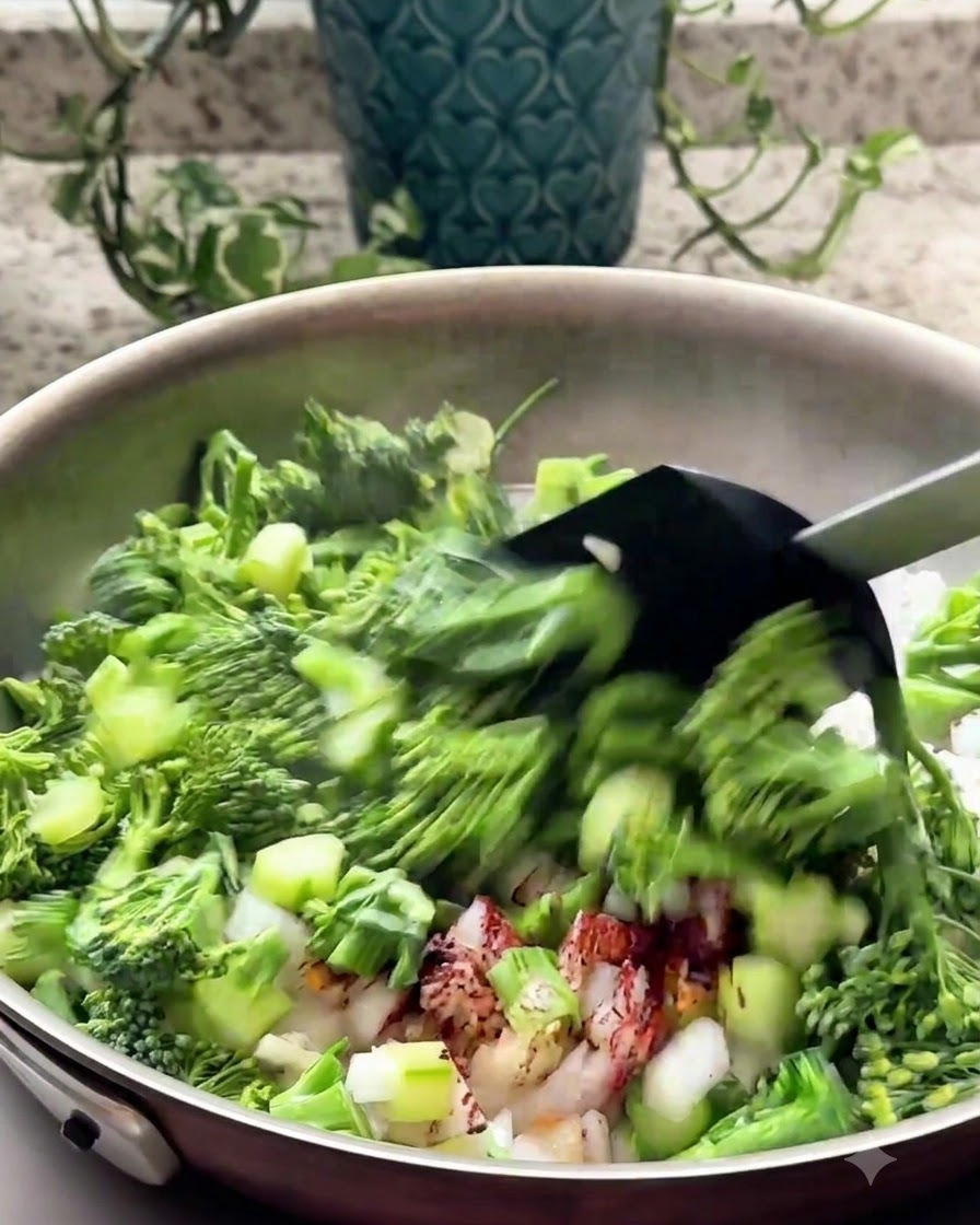 Chopped broccoli and aromatics being stir-fried in a pan with a black spatula.