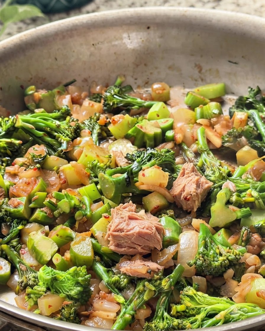 Chunks of canned tuna mixed into the pan with green broccoli and onions.