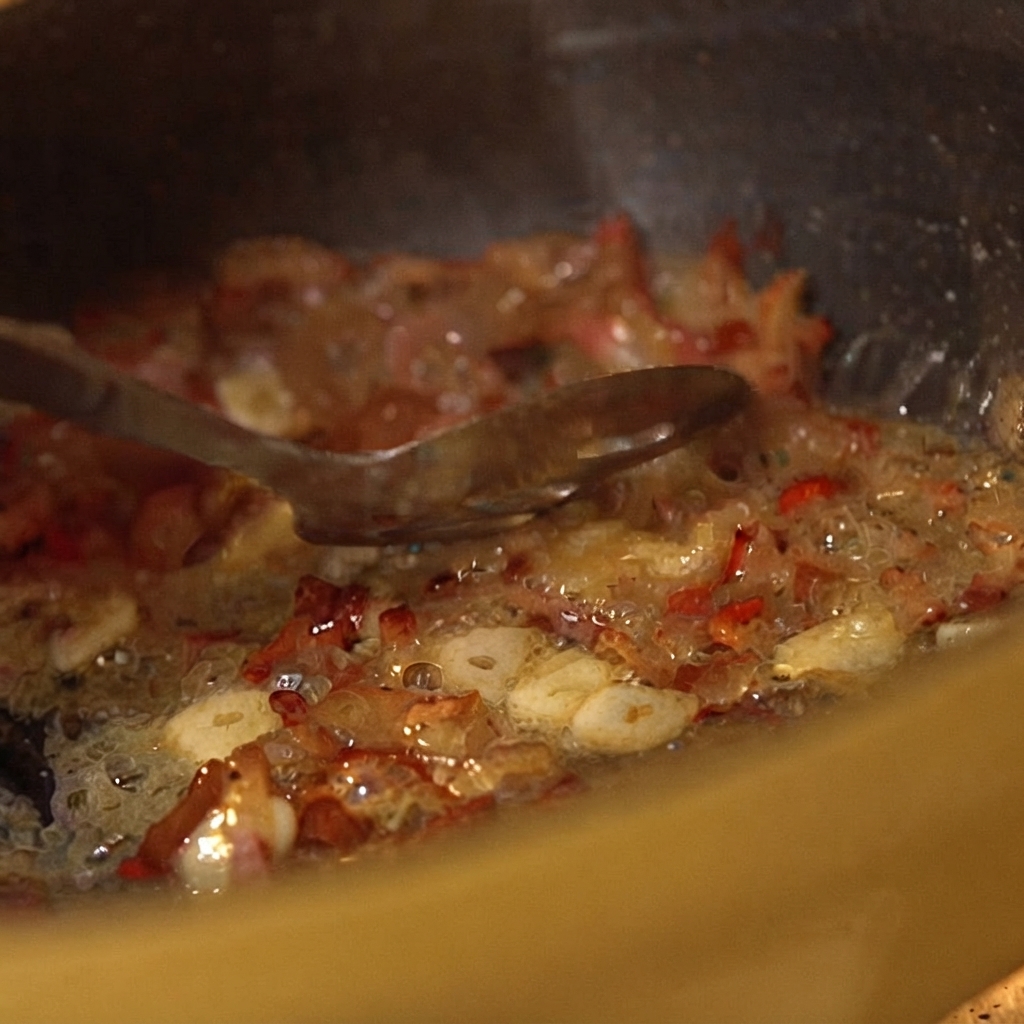Canned crushed tomatoes being mixed into the sizzling pan ingredients with a spoon.