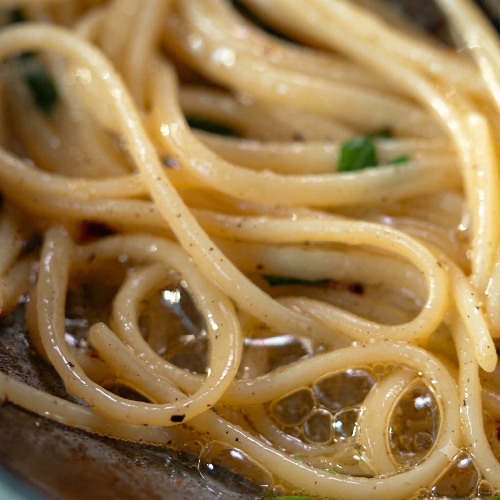 A ladle and tongs lifting and transferring seasoned pasta onto a silver plate.