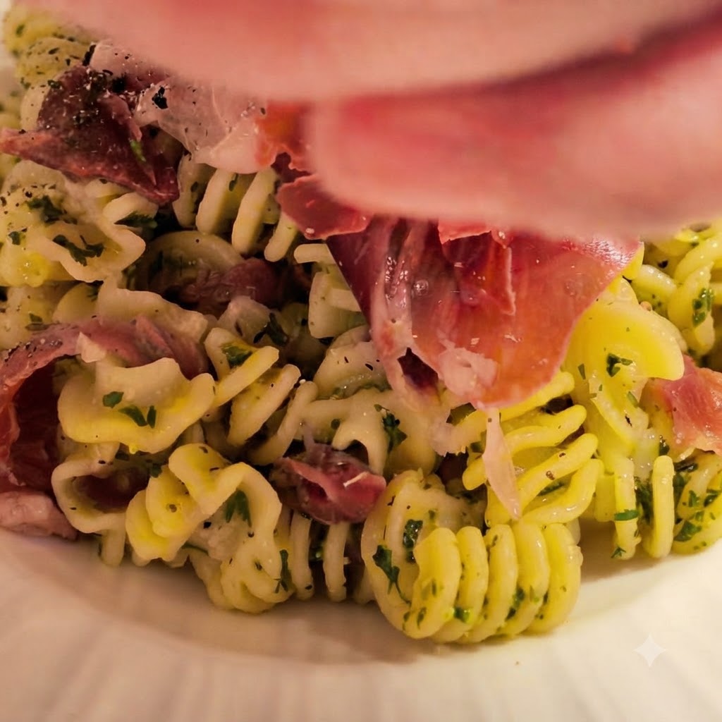 Cooked spiral pasta being tossed into the bowl with the prepared butter and garlic sauce, garnished with fresh herbs and ham.