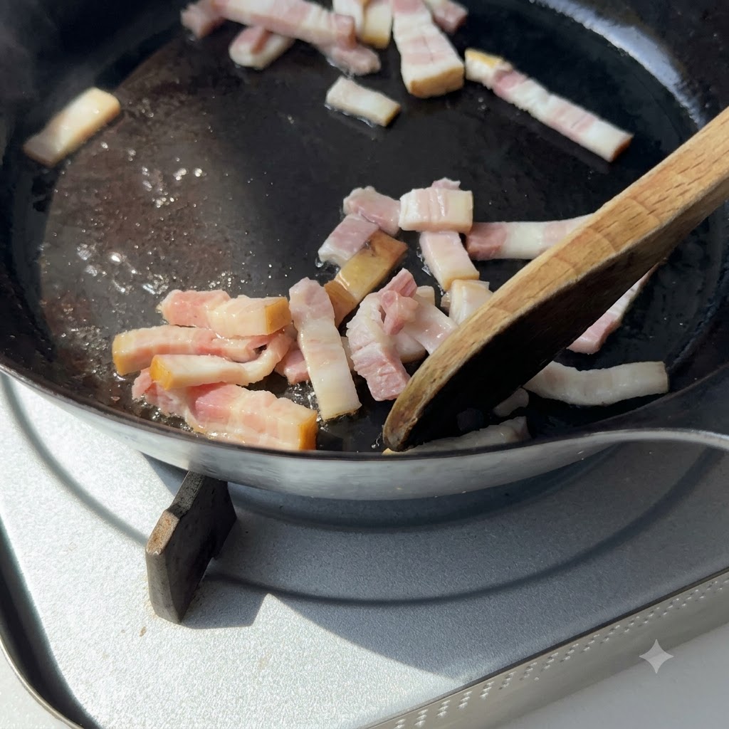 A wooden spatula stirring pieces of bacon in a cast iron skillet over a stovetop.