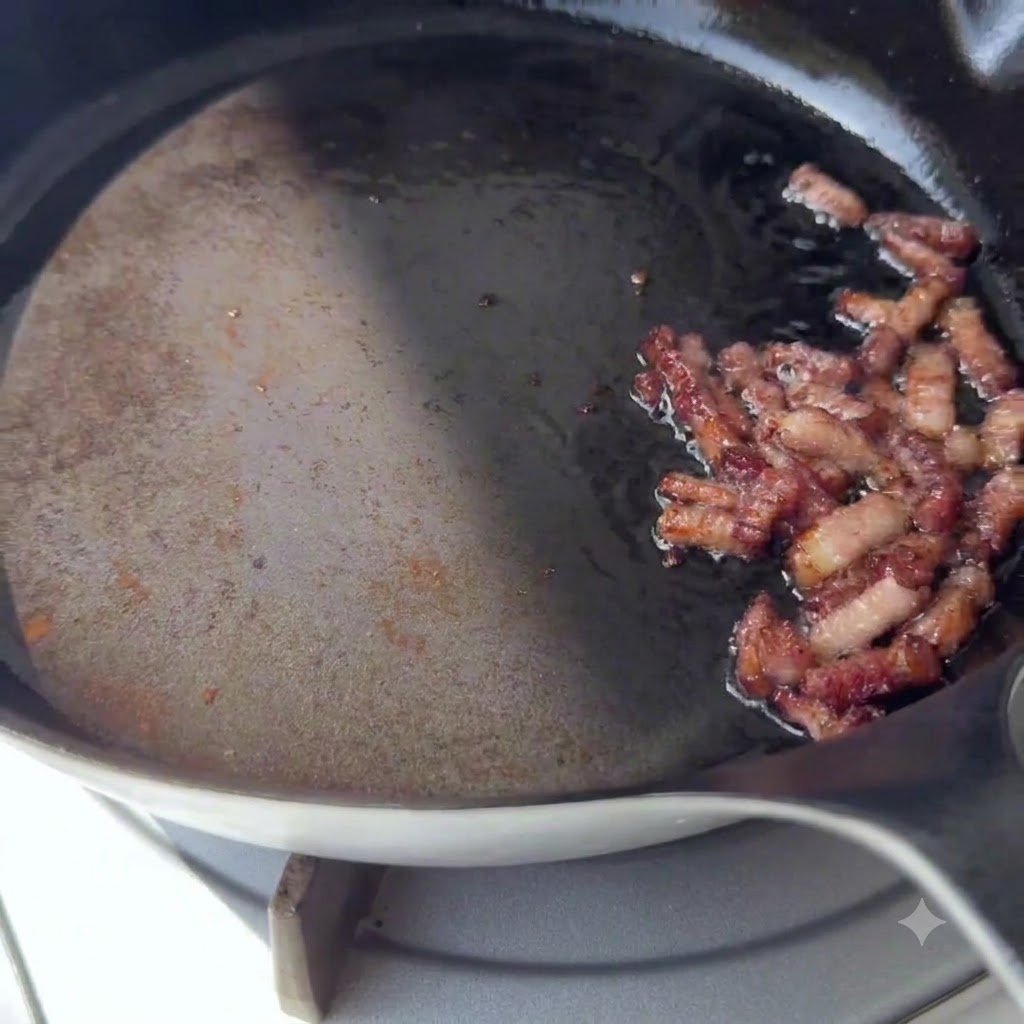 Golden brown bacon pieces sizzling on one side of a hot skillet.
