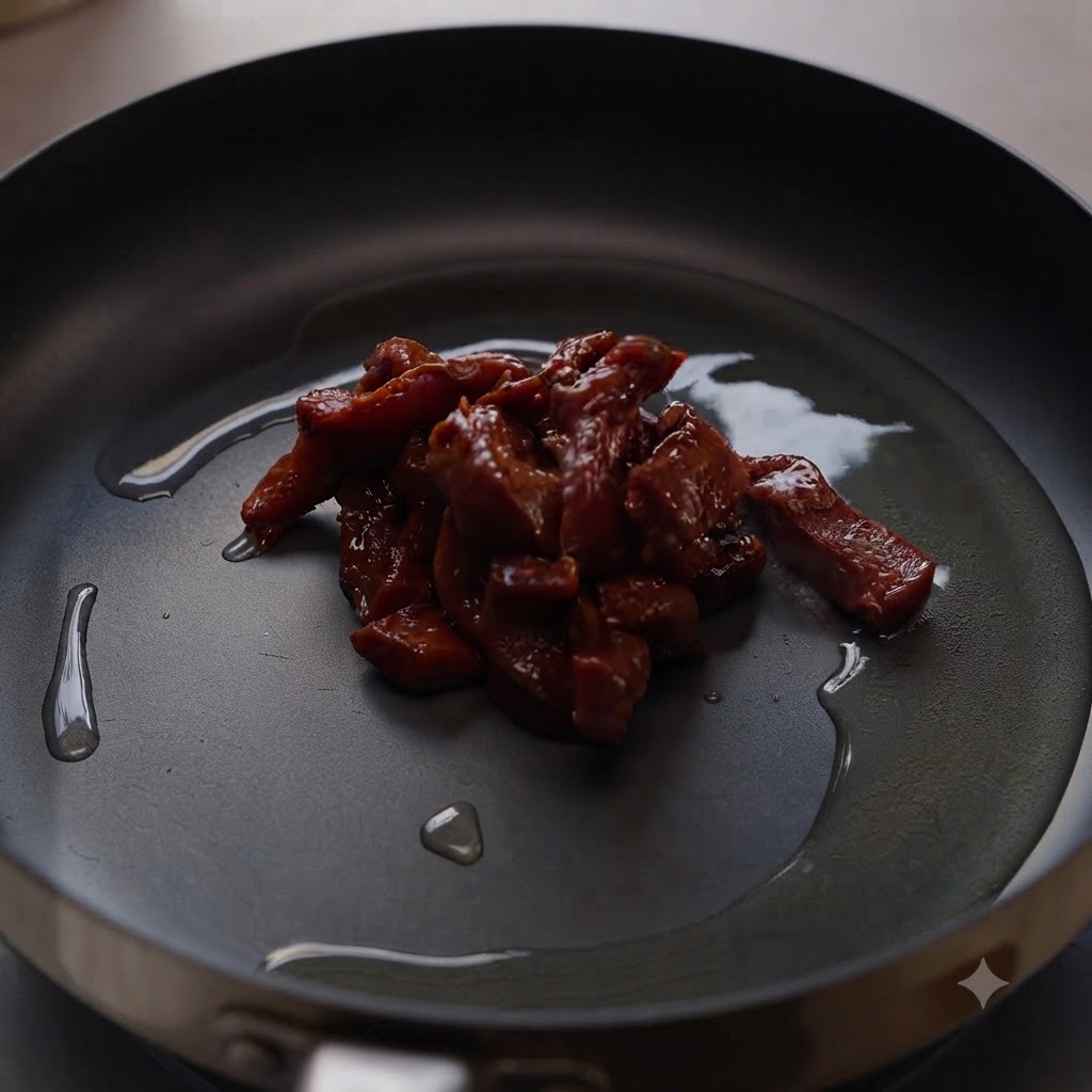 Marinated beef pieces sizzling in the center of a hot frying pan coated with cooking oil.