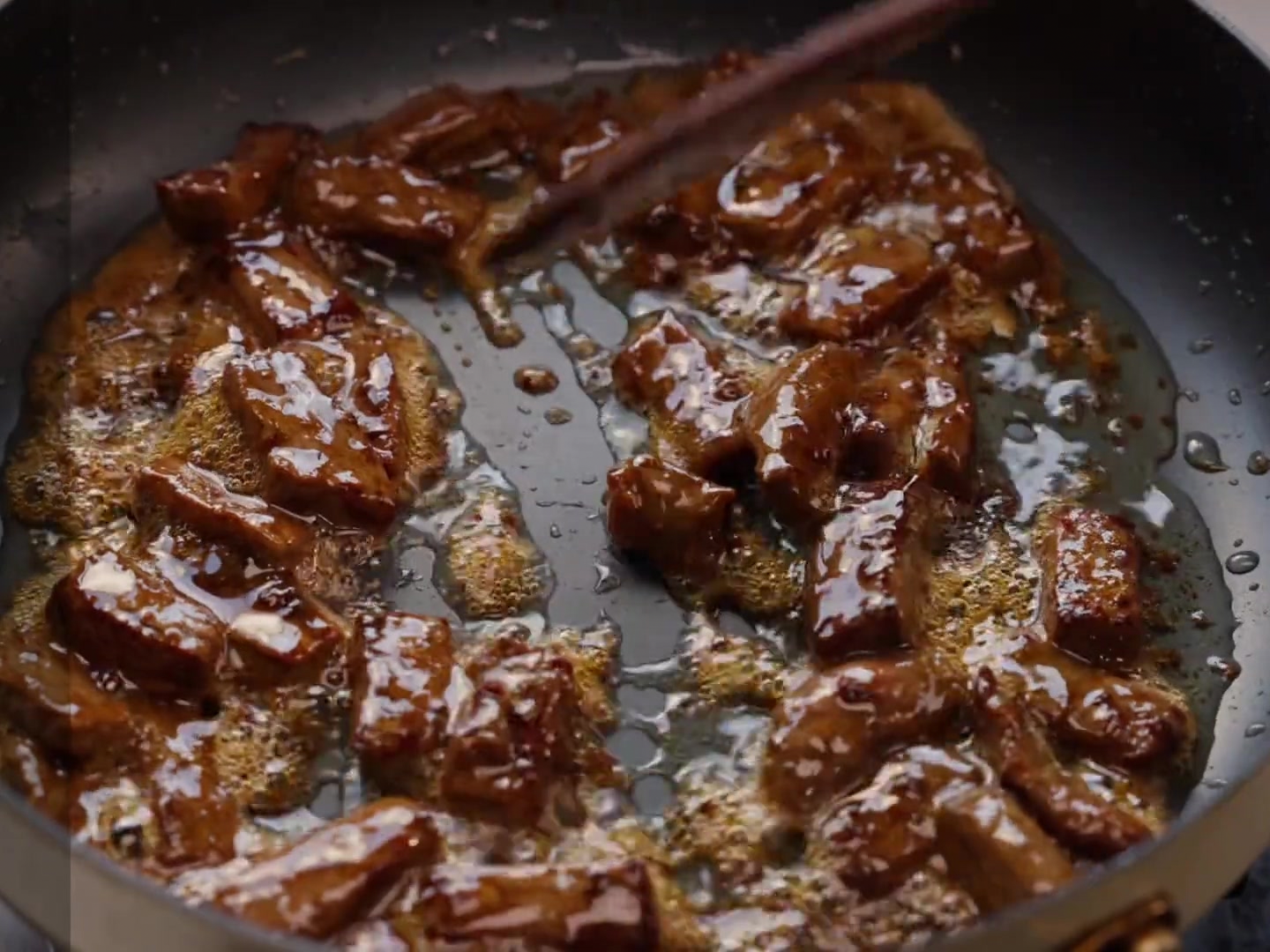 Sliced bell peppers and onions being mixed into a pan of brown steak pieces.