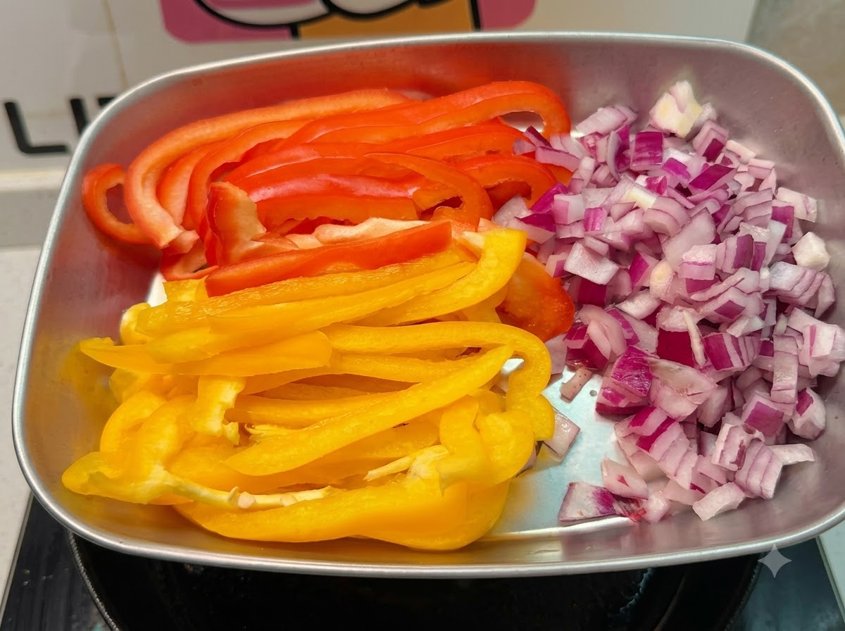 A metal tray holding freshly diced red onions and long strips of red and yellow bell peppers.