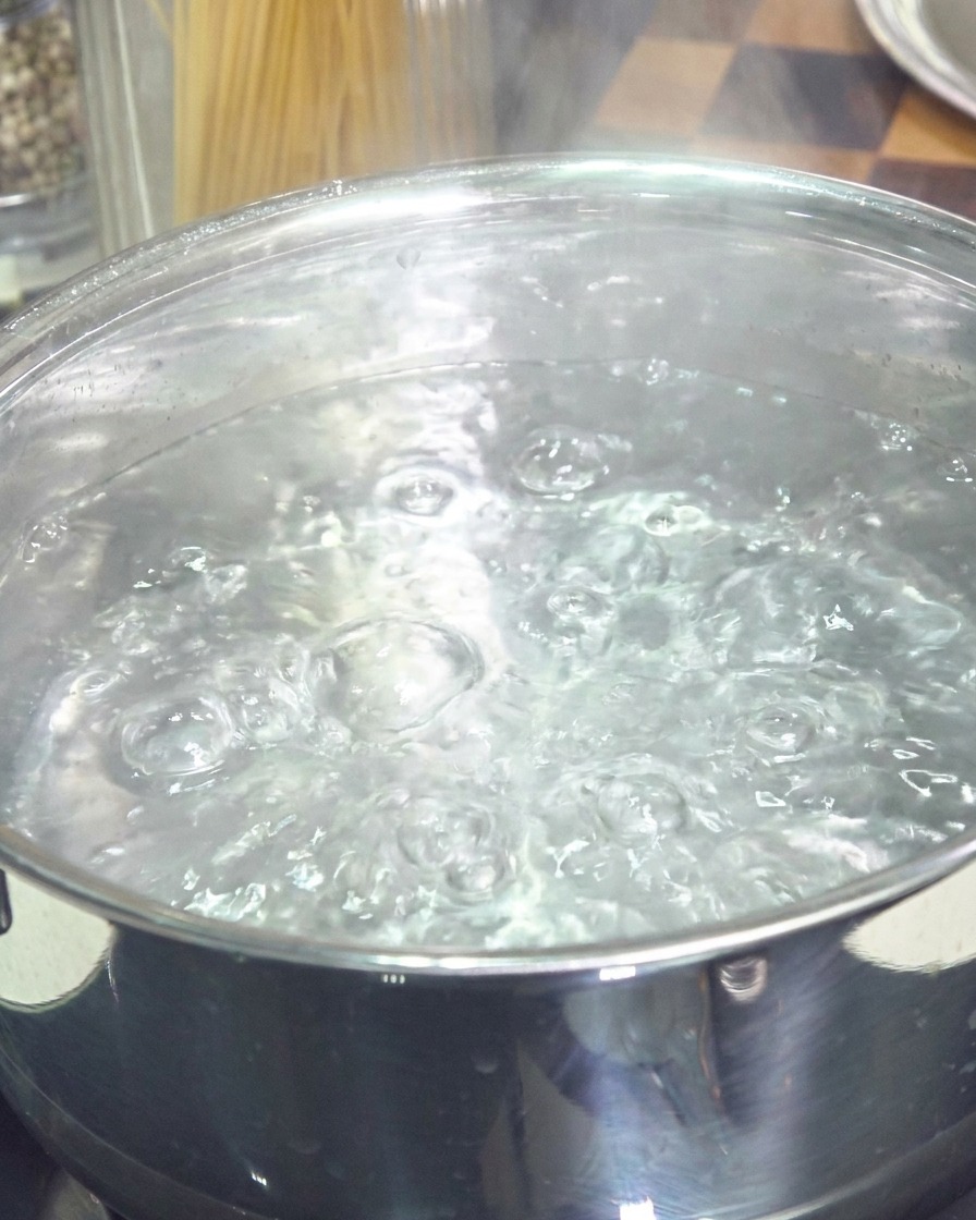 A stainless steel pot filled with vigorously boiling water and bubbles rising to the surface.