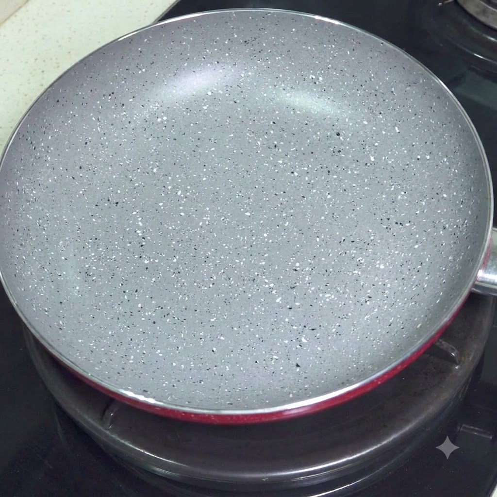 An empty grey speckled non-stick frying pan sitting on a stovetop burner.