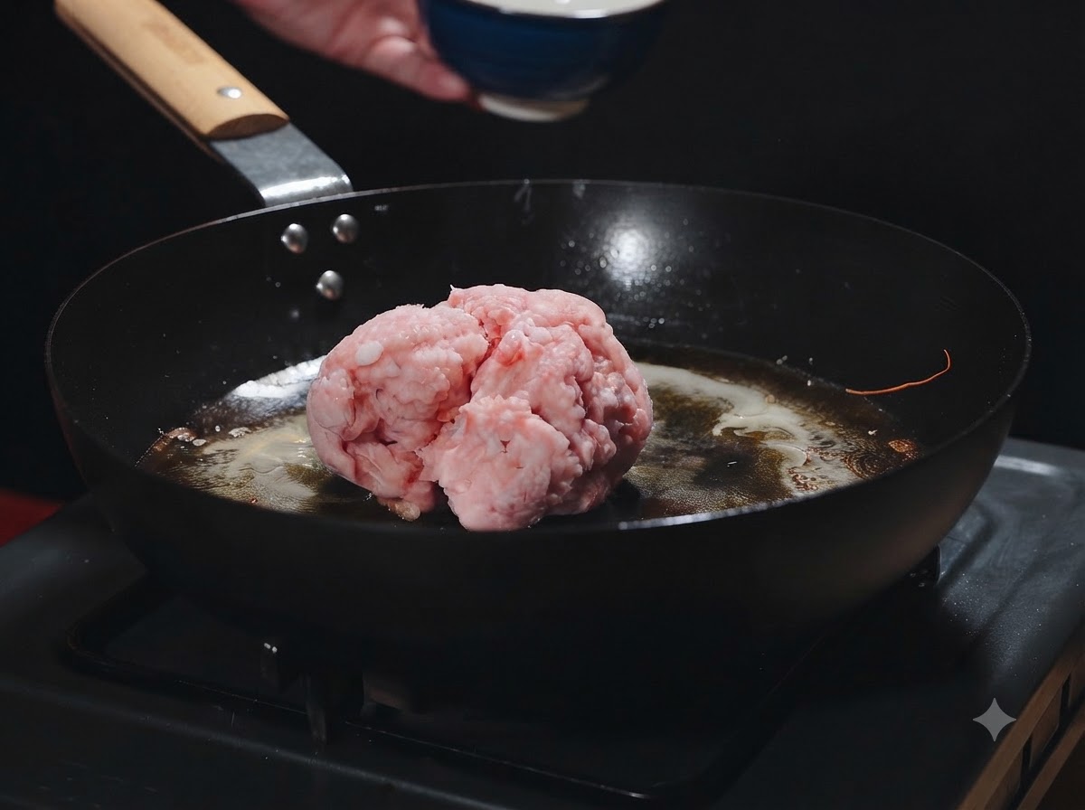 A ball of raw minced meat sitting in a hot pan with shrimp oil while being added.