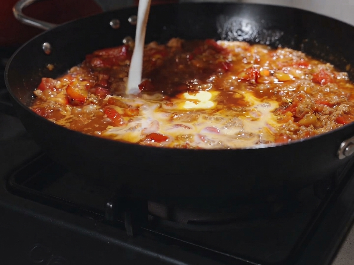 A pat of butter and a splash of milk being poured into the bubbling tomato meat sauce.