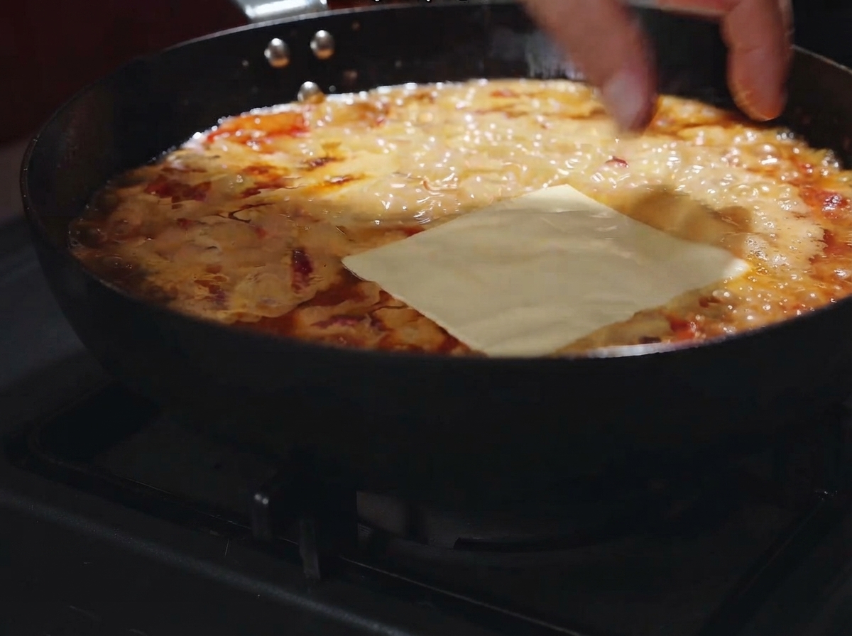 A cheese slice laid flat over the bubbling creamy sauce in the pan.