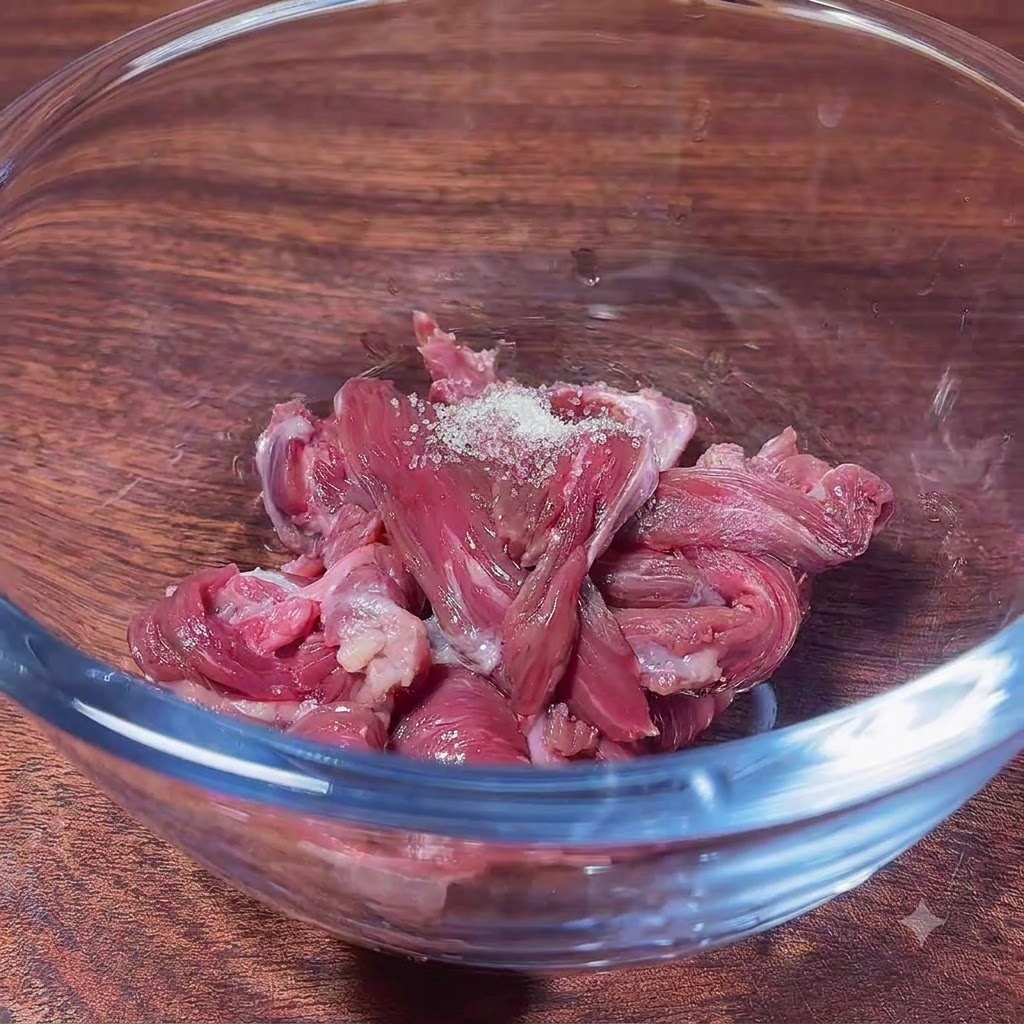 Raw beef slices in a glass bowl topped with sugar, ready to be mixed with marinade ingredients.