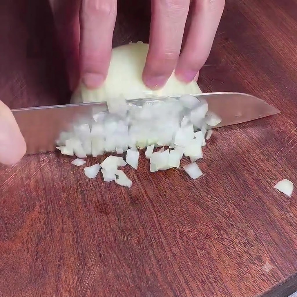 Hands holding a knife to finely dice an onion on a wooden cutting board.