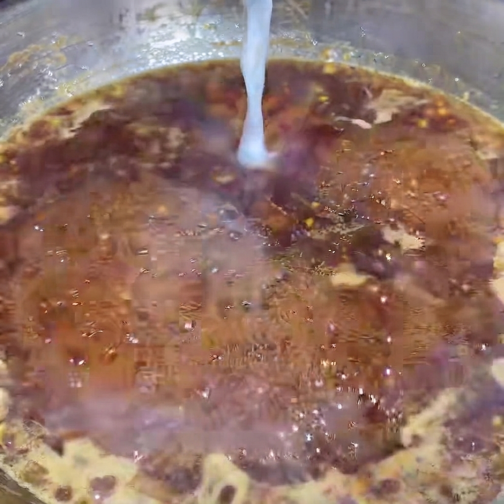 A thin stream of white starch water being poured into a bubbling, dark black pepper sauce in a hot pan.
