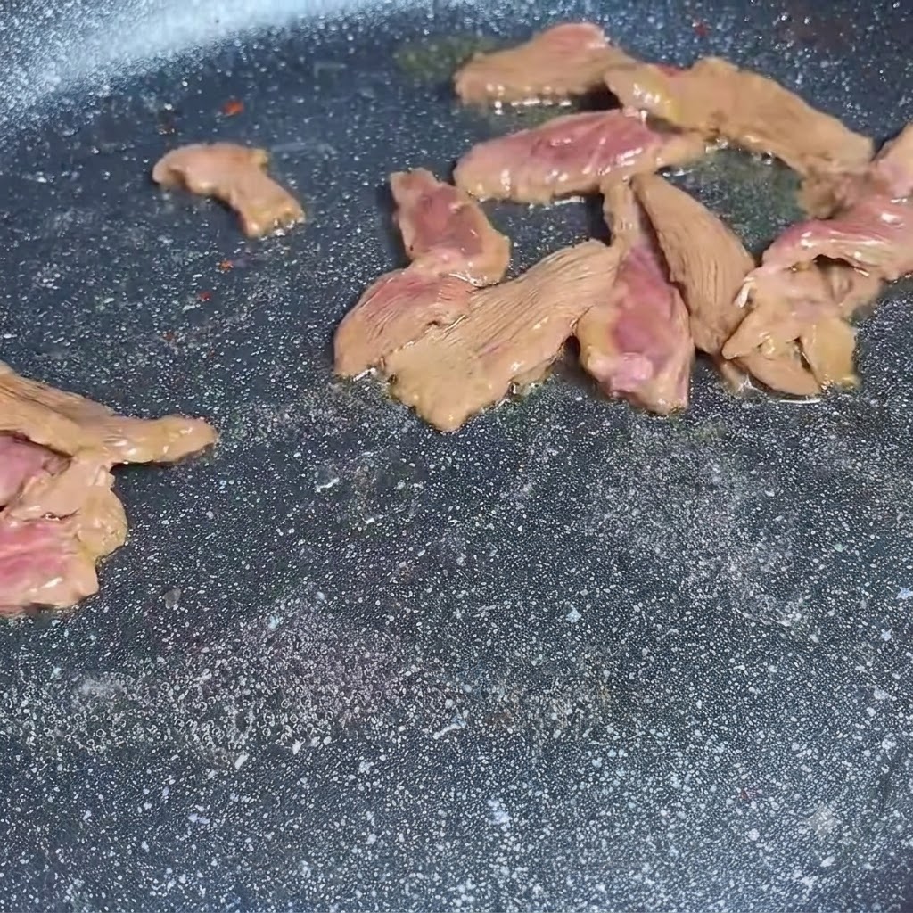 Beef slices being stir-fried in a frying pan.