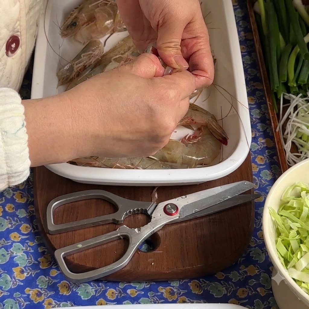 Hands peeling and pulling out the dark vein from a raw shrimp placed on a white tray.