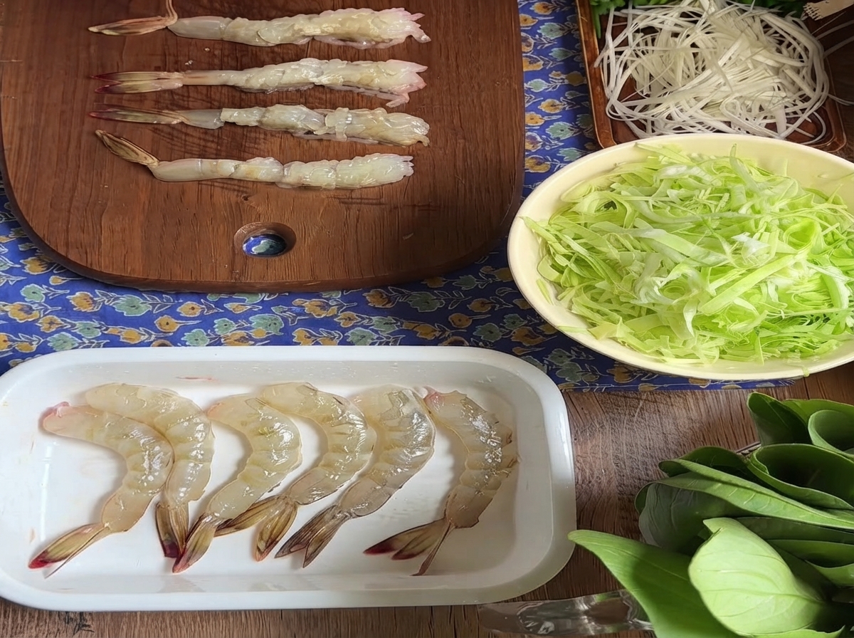 Several raw peeled shrimp lined up on a wooden cutting board after having their belly tendons prepared.
