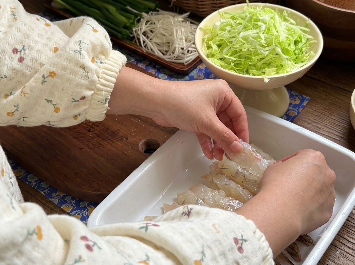 Hands pressing raw shrimp flat in a white tray to prepare them for marinating.