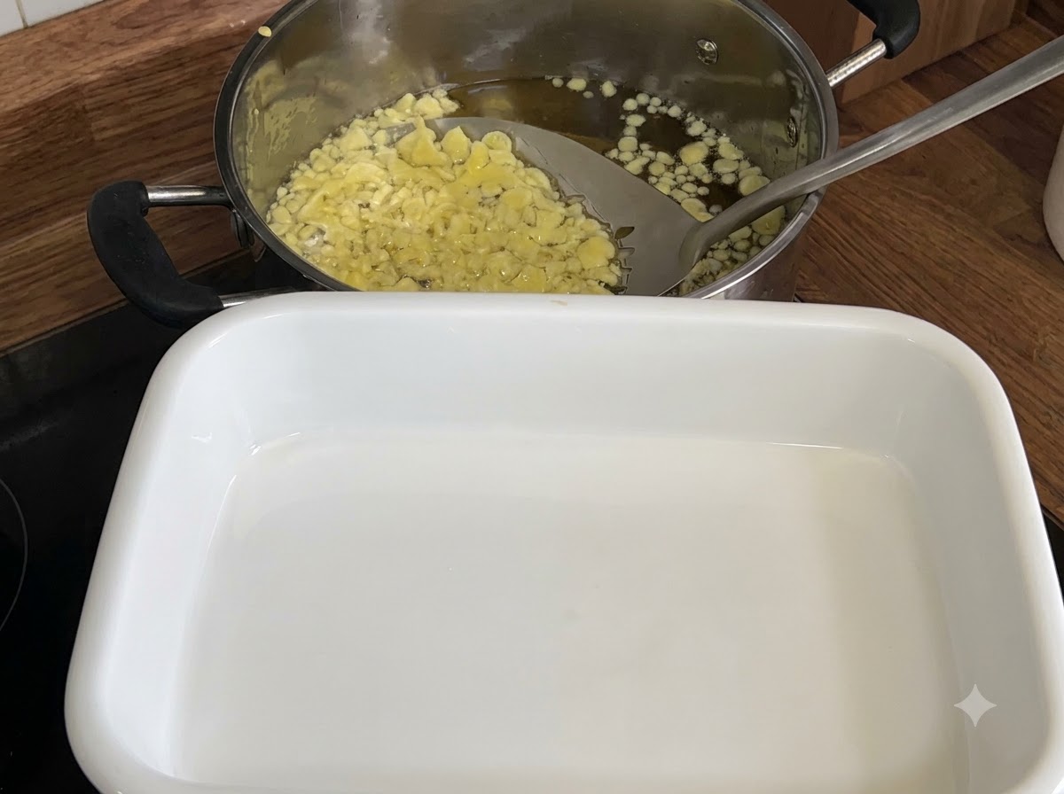 A slotted spoon scooping pale yellow fried tempura flakes from a pot of oil into a white tray.