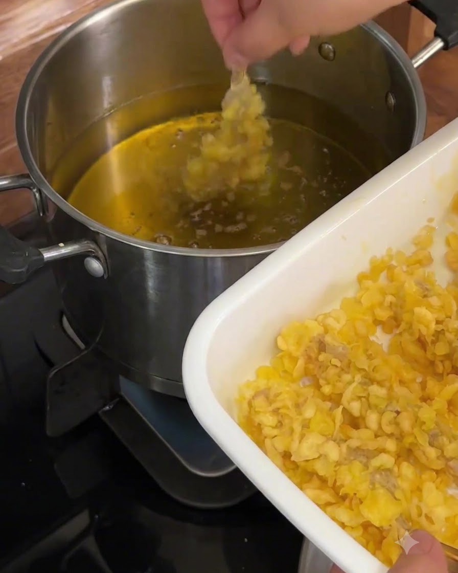 A thickly coated shrimp being lowered into hot oil in a metal pot.