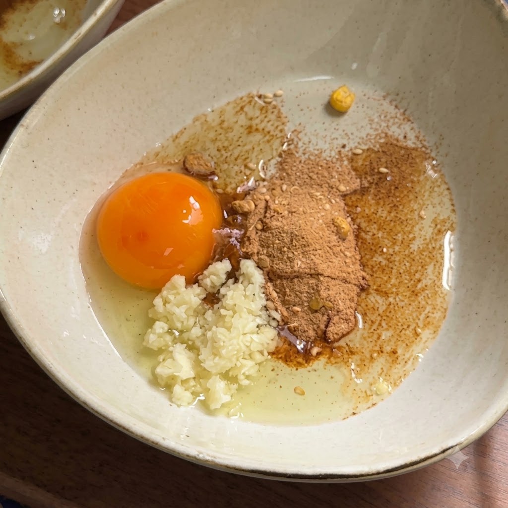 Mayonnaise being squeezed into a bowl with a raw egg yolk, garlic, and seasoning powder.