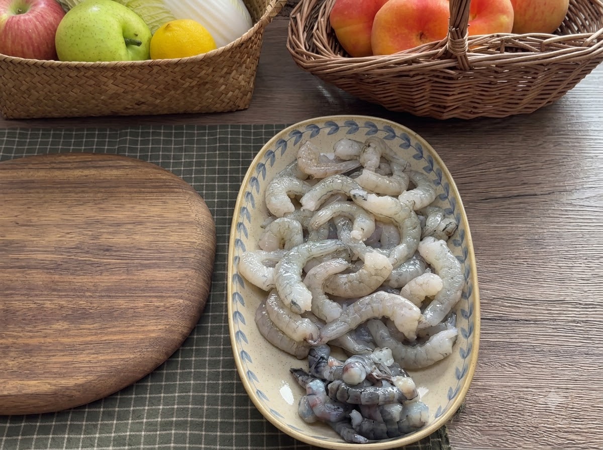 Shrimp meat being chopped on a wooden cutting board with a cleaver into different sizes.