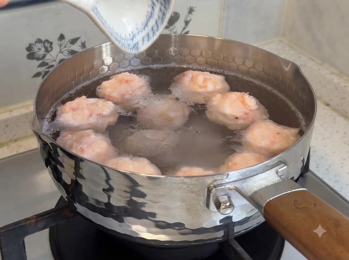 Plump homemade shrimp balls simmering in a pot of warm water on the stovetop.