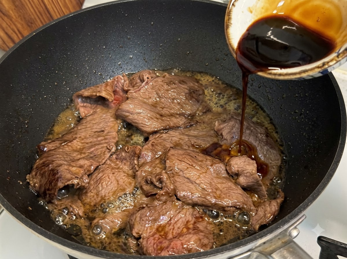 Teriyaki sauce being poured into a pan over sliced fatty beef to simmer and reduce.