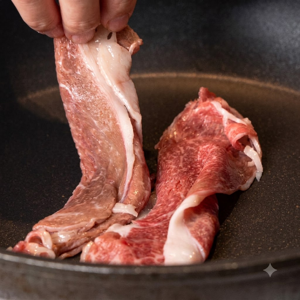 Sliced wagyu beef chuck being placed into a dry, heated non-stick pan.